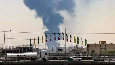 Flags flutter along a bridge as a plume of heavy smoke and fire rise from an oil refinery in southern Tehran, after it was hit in an overnight Israeli strike. (AFP) Flags flutter along a bridge as a plume of heavy smoke and fire rise from an oil refinery in southern Tehran, after it was hit in an overnight Israeli strike. (AFP)