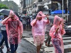 Commuters wearing raincoats and holding umbrellas cross a road amid rains in Mumbai.