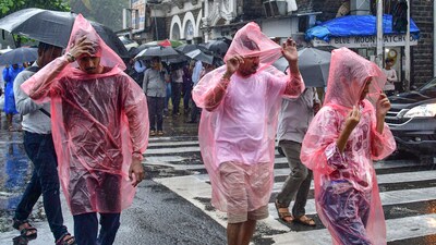 Commuters wearing raincoats and holding umbrellas cross a road amid rains in Mumbai. (PTI) Commuters wearing raincoats and holding umbrellas cross a road amid rains in Mumbai. (PTI)