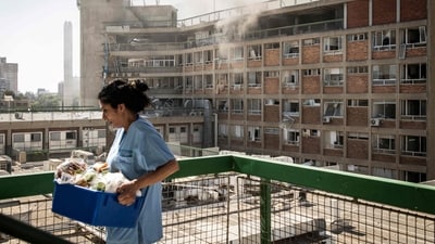 A nurse carries medical supplies past a building with smoke billowing out after at Soroka Hospital after it was struck. (AFP) A nurse carries medical supplies past a building with smoke billowing out after at Soroka Hospital after it was struck. (AFP)