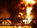 People watch from a bridge as flames from an Israeli attack rise from Sharan Oil depot, following Israeli strikes on Iran, in Tehran.