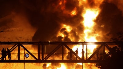 People watch from a bridge as flames from an Israeli attack rise from Sharan Oil depot, following Israeli strikes on Iran, in Tehran. (Reuters file photo)