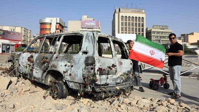 A man holds an Iranian flag by an Iranian Red Crescent ambulance that was destroyed during an Israeli strike, displayed in Tehran on June 23,2025. (AFP) A man holds an Iranian flag by an Iranian Red Crescent ambulance that was destroyed during an Israeli strike, displayed in Tehran on June 23,2025. (AFP)