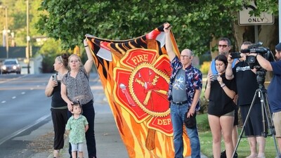 People pay their respects as they wait for a procession from Kootenai Health to pass by on its way to the medical examiner's office in Spokane, Wash., after firefighters were killed in a sniper attack Sunday, June 29, 2025, while they were responding to a blaze near Coeur d’Alene, Idaho. (Bill Buley/Coeur D'Alene Press via AP) (AP) People pay their respects as they wait for a procession from Kootenai Health to pass by on its way to the medical examiner's office in Spokane, Wash., after firefighters were killed in a sniper attack Sunday, June 29, 2025, while they were responding to a blaze near Coeur d’Alene, Idaho. (Bill Buley/Coeur D'Alene Press via AP) (AP)