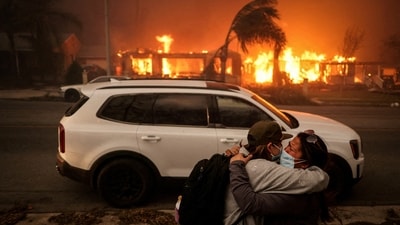 People embrace each other as they evacuate following devastating wildfires in the Los Angeles area, at the Eaton Fire in Altadena, California. (Reuters)