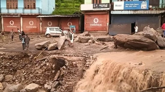 People stand near silt and debris after cloudburst-triggered flash floods at Karsog, in Mandi district, (PTI)