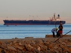 People walk on the beach as a container ship crosses the Gulf of Suez towards the Red Sea before entering the Suez Canal.