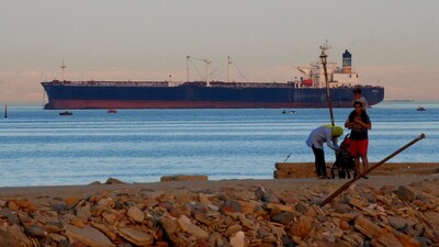 People walk on the beach as a container ship crosses the Gulf of Suez towards the Red Sea before entering the Suez Canal. (For representation/Reuters)