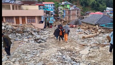 Locals carry their belongings as they walk amid the debris at a flood-affected area, at Thunag in Mandi district on Monday. (PTI) Locals carry their belongings as they walk amid the debris at a flood-affected area, at Thunag in Mandi district on Monday. (PTI)