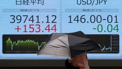 A woman holding a sunshade walks in front of a screen displaying Japan's Nikkei share average and exchange rate between Japanese yen and US dollar outside a brokerage in Tokyo (REUTERS)