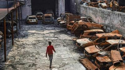 New Delhi: A man walks past the charred remains of vehicles set ablaze by rioters at parking during the anti-CAA protests in February at Shiv Vihar area of Northeast Delhi (PTI) New Delhi: A man walks past the charred remains of vehicles set ablaze by rioters at parking during the anti-CAA protests in February at Shiv Vihar area of Northeast Delhi (PTI)
