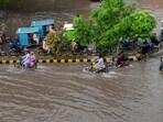 Commuters cross a flooded street after heavy monsoon rains in Lahore on July 9, 2025.