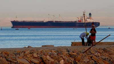 People walk on the beach as a container ship crosses the Gulf of Suez towards the Red Sea before entering the Suez Canal. (Reuters)