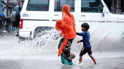 A mother with her two kids crosses the road amid rain and splashes, in Rajasthan's Bikaner. (ANI) A mother with her two kids crosses the road amid rain and splashes, in Rajasthan's Bikaner. (ANI)
