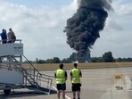 A plume of black smoke rises from an area near the runway after a small plane crash, as seen from inside a building at London Southend Airport, in Southend.