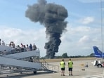 A plume of black smoke rises from an area near the runway after a small plane crash, as seen from inside a building at London Southend Airport.