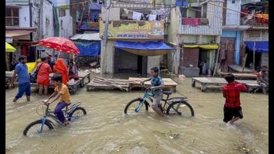 Children ride bicycles in an area inundated with water of the swollen Ganga river, in Prayagraj, Friday. (PTI Photo)