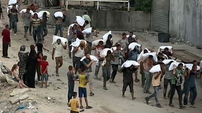 Men walk carrying sacks of flour that were taken from a raided truck carry sacks of flour after raiding a truck that was carrying foodstuffs, in Khan Yunis in the southern Gaza Strip on July 22, 2025. (AFP)