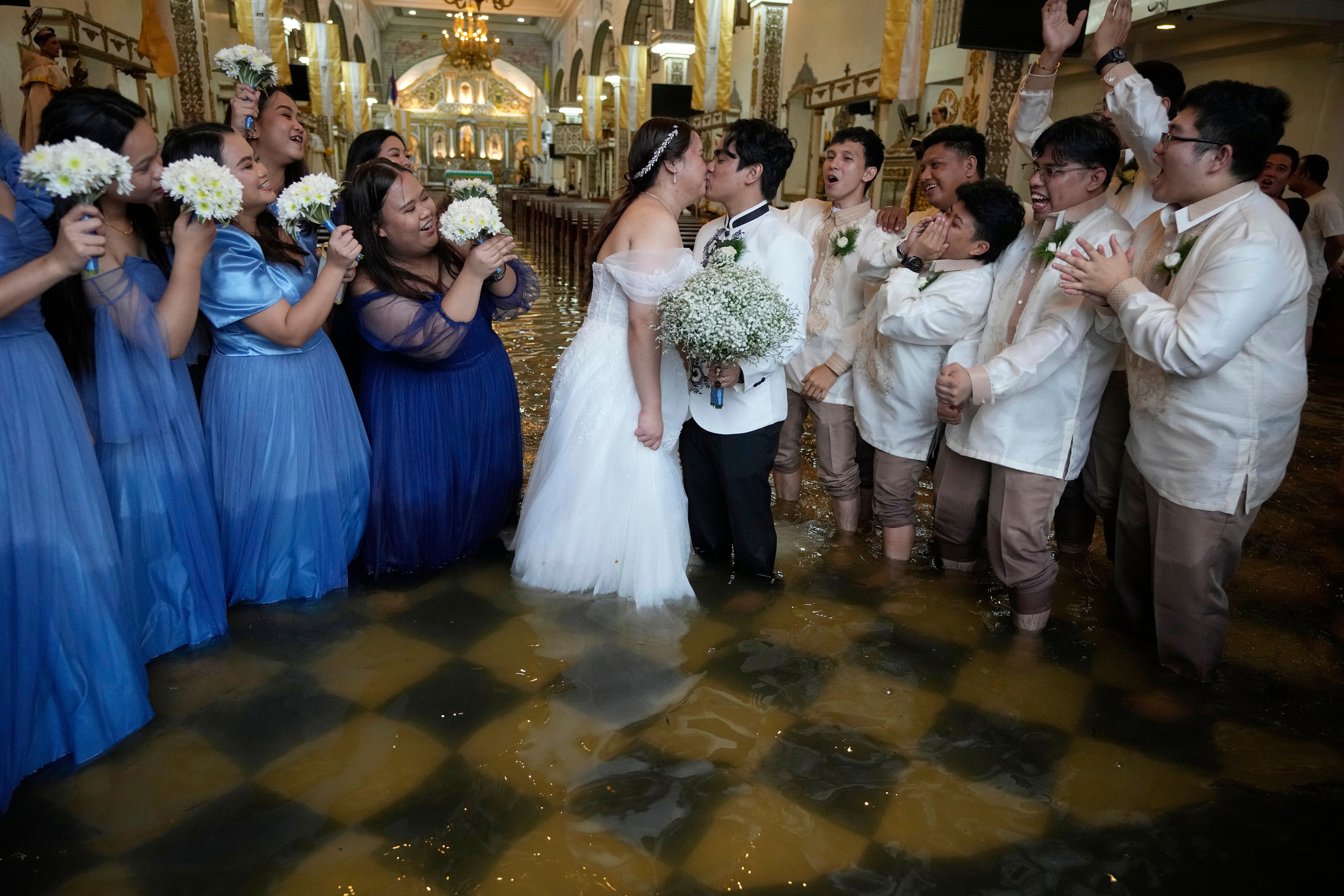 Newlyweds Jade Rick Verdillo, center, and Jamaica pose with a kiss as guests cheer at the flooded Barasoain church in Malolos, Bulacan province, Philippines on Tuesday, July 22, 2025. (AP Photo/Aaron Favila) (AP) Newlyweds Jade Rick Verdillo, center, and Jamaica pose with a kiss as guests cheer at the flooded Barasoain church in Malolos, Bulacan province, Philippines on Tuesday, July 22, 2025. (AP Photo/Aaron Favila) (AP)