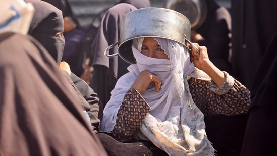 A Palestinian woman shields herself from the sun with her pot as she waits with others for a meal at a charity kitchen in the Mawasi area of Khan Yunis in the southern Gaza Strip.(AFP)