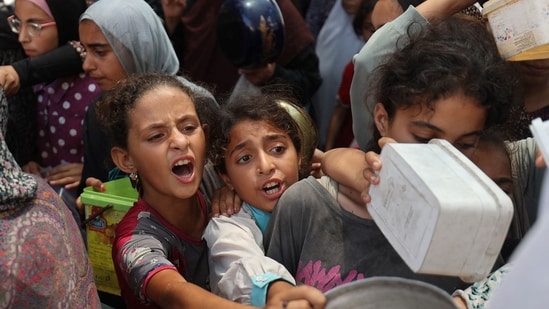 Palestinian children queue for a portion of hot food distributed by a charity kitchen at the Nuseirat refugee camp in the central Gaza Strip.(AFP)