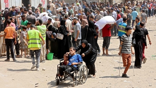 A Palestinian woman pushes a man and child on a wheelchair as people gather to receive bags of flour at a UN World Food Programme (WFP) warehouse on Al-Jalaa street in Gaza City.(AFP)