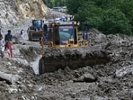 Local residents walk past bulldozers removing debris to clear the way at a site of landslides triggered by flash floods following heavy monsoon rains, on a highway near the Chilas district, northern Pakistan, Friday, July 25, 2025.