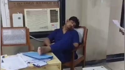 The screengrab from the video shows a doctor reclining with their legs up in front of an air conditioner, visibly asleep. (X) The screengrab from the video shows a doctor reclining with their legs up in front of an air conditioner, visibly asleep. (X)