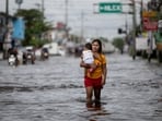A woman carrying a baby wades through a flooded area in Manila North Road following heavy rains brought by Typhoon Co-may in Minalin, Pampanga, Philippines. The storm is now expected to head to Shanghai.