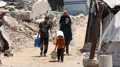 A Palestinian child shields his head with a bucket while hauling precious water from a distribution point through Gaza City, joining others in their daily struggle for survival. (Omar Al-Qattaa/AFP)