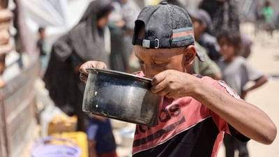 An emaciated Palestinian boy drinking scarce lentil soup procured from a distribution center. (Omar Al-Qattaa/AFP)