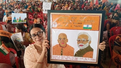 A woman holds a portrait of Prime Minister Narendra Modi and Uttar Pradesh CM Yogi Adityanath that was made by children using rice and pulses. (PTI) A woman holds a portrait of Prime Minister Narendra Modi and Uttar Pradesh CM Yogi Adityanath that was made by children using rice and pulses. (PTI)