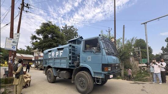 A CRPF vehicle moving past people standing on a roadside during an encounter between terrorists and security forces in the Akhal area of Kulgam district on Saturday. (PTI Photo)