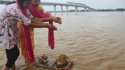 Two women stand amid the swollen Ganga, as they offer the flooded water on an almost submerged Shivling, along the submerged banks of the river. (Rajesh Kumar/HT)