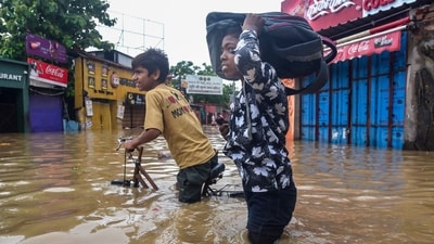 A young boy carries his schoolbag on his head and the other paddles his bicycle as the two wade their way through a waterlogged street in Varanasi. (PTI)