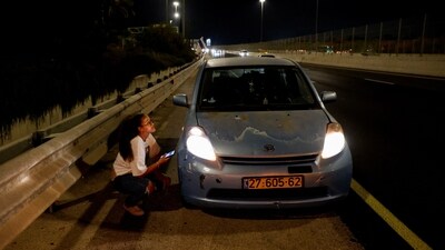 A woman takes cover behind a car, which stopped at the side of a road, while sirens sound, in response to what the Israeli military reported was a missile launched from Yemen towards Israel that was intercepted, in Tel Aviv, Israel, July 29, 2025. (Reuters)
