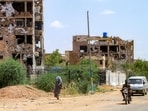 A woman walks past motorists driving near heavily-damaged buildings in the Lamab suburb on the southwestern outskirts of Sudan's capital Khartoum on July 30 A woman walks past motorists driving near heavily-damaged buildings in the Lamab suburb on the southwestern outskirts of Sudan's capital Khartoum on July 30