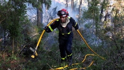 A firefighter carries a fire hose during a wildfire near Saint-Laurent-de-la-Cabrerisse, southern France. (REUTERS)