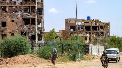 A woman walks past motorists driving near heavily-damaged buildings in the Lamab suburb on the southwestern outskirts of Sudan's capital Khartoum on July 30 (AFP) A woman walks past motorists driving near heavily-damaged buildings in the Lamab suburb on the southwestern outskirts of Sudan's capital Khartoum on July 30 (AFP)
