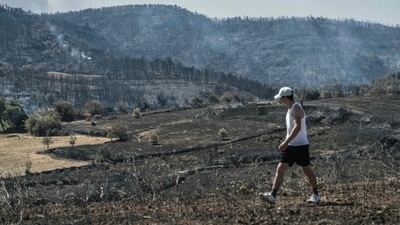A man walks through a scorched area as smoke billows in the background during a wildfire in Saint-Laurent-de-la-Cabrerisse, southwestern France. (AFP) A man walks through a scorched area as smoke billows in the background during a wildfire in Saint-Laurent-de-la-Cabrerisse, southwestern France. (AFP)