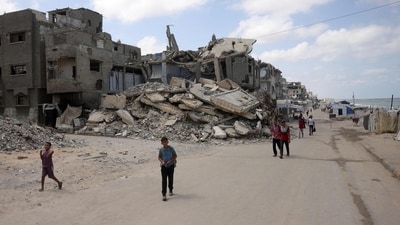 Palestinians walk along a street near war-damaged buildings along the shore in Gaza City. (AFP)