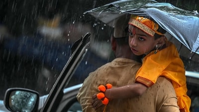 A man carries his son dressed as the Hindu god Krishna ahead of Janmashtami celebrations during rainfall in New Delhi. (AFP)