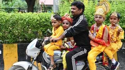 A man rides a bike with children dressed as Lord Krishna for Janmashtami festival celebrations in Prayagraj. (Nitin Sharma/ANI)