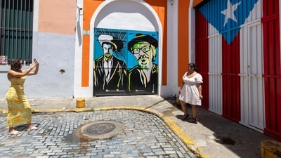 Tourists takes phots next to a mural featuring Bad Bunny and Elizam Escobar in Old San Juan, Puerto Rico, as Hurricane Erin approaches, Friday, Aug. 15, 2025. (AP Photo/Alejandro Granadillo) (AP)