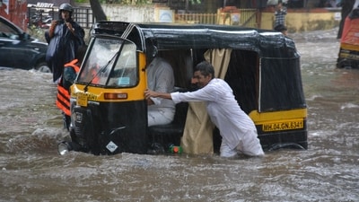An auto-rickshaw driver helps his fellow navigate through knee-deep water on a road in Thane after heavy rain caused widespread waterlogging in the region. (Praful Gangurde/Hindustan Times)