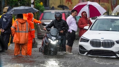 A car wades through a waterlogged road in Mumbai's Dadar while relief personnel stand with their umbrellas, a commuter walks his bike and others stand with trousers rolled up. (Kunal Patil/PTI) A car wades through a waterlogged road in Mumbai's Dadar while relief personnel stand with their umbrellas, a commuter walks his bike and others stand with trousers rolled up. (Kunal Patil/PTI)