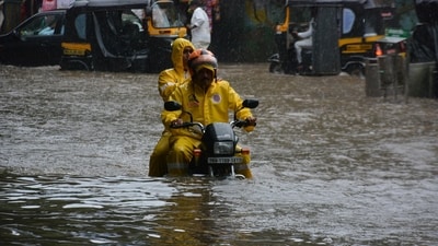 Two Mumbai Police personnel make their way through a waterlogged road near Vandana Cinema in Thane as rain battered the city. (Praful Gangurde/Hindustan Times)