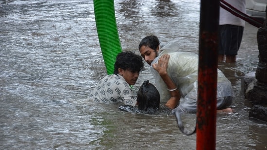 Commuters stuck in a waterlogged road in Thane help each other.(Praful Gangurde/Hindustan Times)