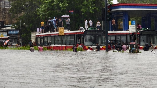 People climb onto the roof of buses moving through a waterlogged road amid rainfall at Kurla in Mumbai after heavy rainfall on Tuesday. (Raju Shinde/HT Photo)