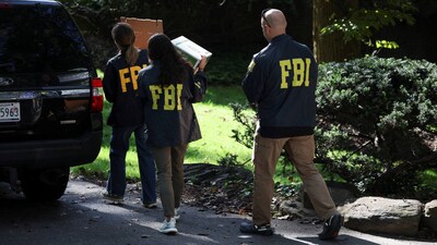FBI members carry boxes outside the home of the former White House national security adviser John Bolton on Friday. FBI members carry boxes outside the home of the former White House national security adviser John Bolton on Friday.